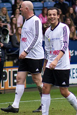 Two men walking together on a football field, wearing a black and white football kit.