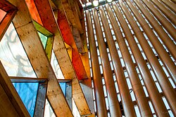Close-up architectural details showing cardboard tubes, wooden elements, and colored glass panels in clear, red, yellow, green, and blue