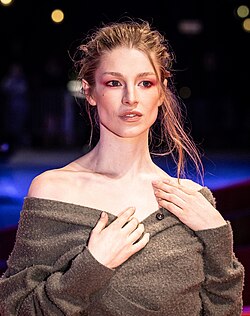 Headshot of Hunter Schafer, a young, white woman with dark blonde hair, wearing a gray off-the-shoulder cardigan.