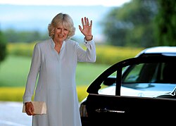 A smiling Camilla waves her hand.